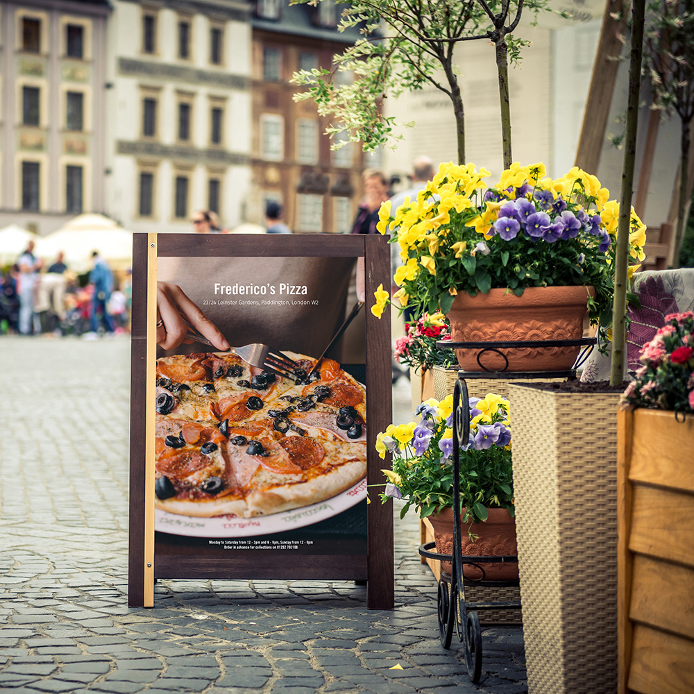 a picture of an outdoor display for a pizza restaurant next to flowers on a street